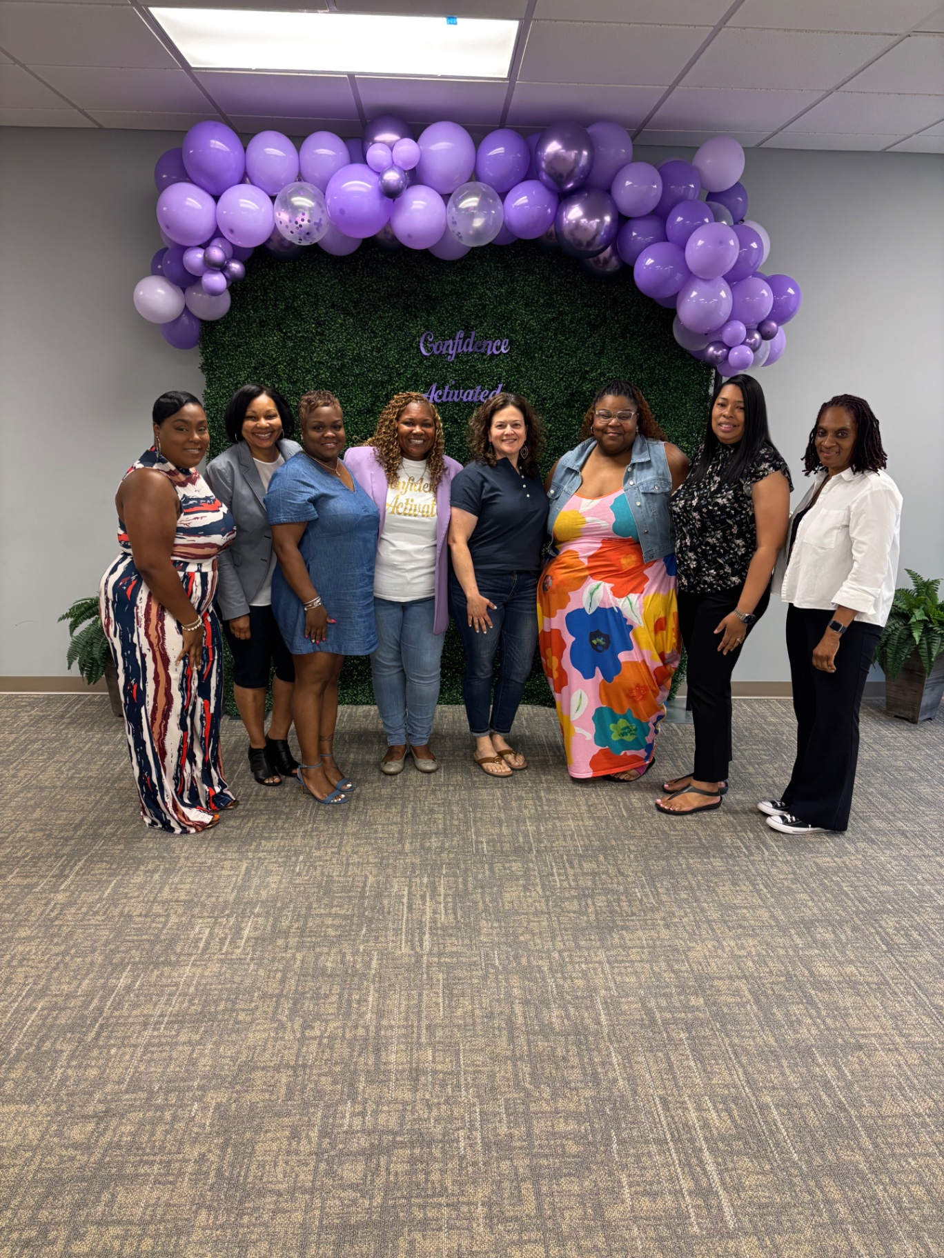 Group photo of women at a Confidence Activated gathering in front of the purple balloon backdrop